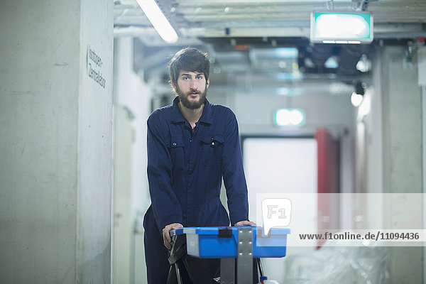 Junges männliches Reinigungspersonal steht mit einem Mülleimer in einer Industrieanlage