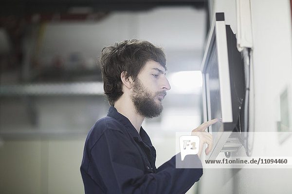 Junger männlicher Ingenieur bei der Arbeit an einem Touchscreen-Computermonitor in einer Industrieanlage