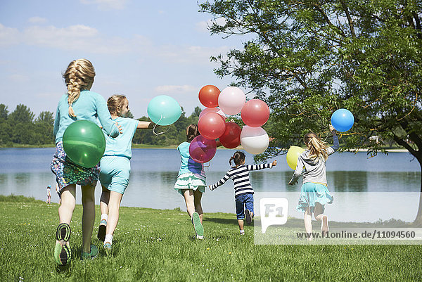 Rückansicht von Mädchen  die im Park mit Luftballons laufen  Karlsfelder See  München  Bayern  Deutschland