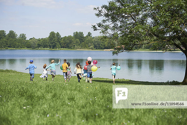 Rückansicht von Kindern  die im Park mit Luftballons laufen  Karlsfelder See  München  Bayern  Deutschland