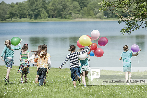 Rückansicht von Kindern,  die im Park mit Luftballons laufen,  München,  Bayern,  Deutschland