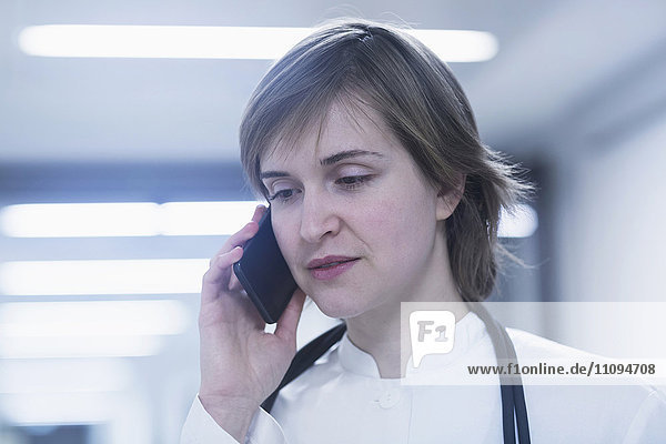 Junge Ärztin,  die in einem Krankenhauskorridor mit einem Mobiltelefon spricht