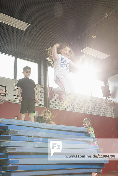 Kinder springen von einem Stapel Sportmatten in einer Sporthalle  München  Bayern  Deutschland