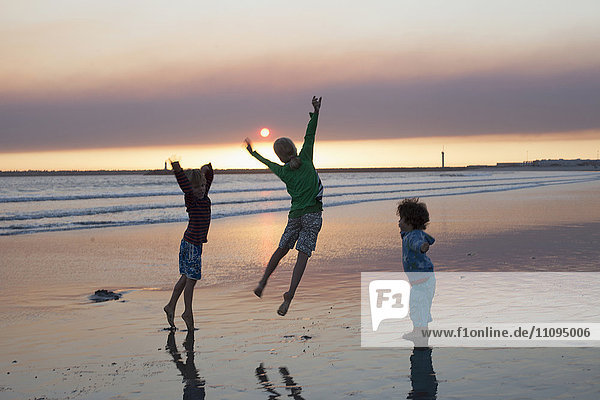 Drei Kinder springen bei Sonnenuntergang am Strand  Viana do Castelo  Region Norte  Portugal