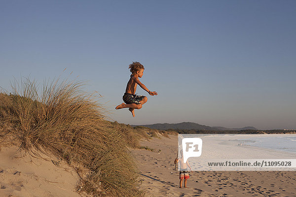 Kleiner Junge springt von einer Sanddüne am Strand  Viana do Castelo  Region Norte  Portugal