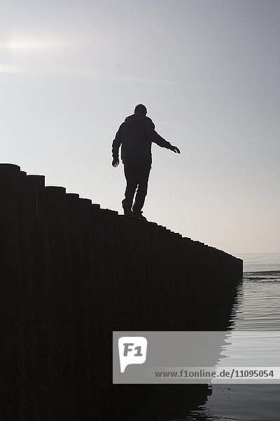 Silhouette eines reifen Mannes  der auf einem Holzpfosten am Strand balanciert  Renesse  Schouwen-Duiveland  Zeeland  Niederlande