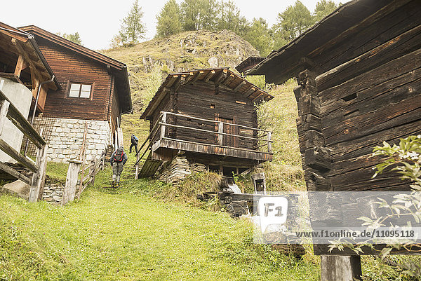 Rückansicht zweier erwachsener Wanderer  die an Hütten vorbeigehen  Österreichische Alpen  Kärnten  Österreich