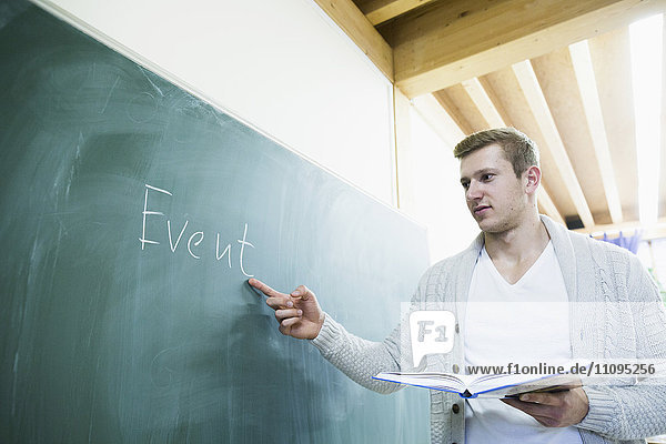 Young male teacher explaining on blackboard in classroom  Freiburg Im Breisgau  Baden-Württemberg  Germany