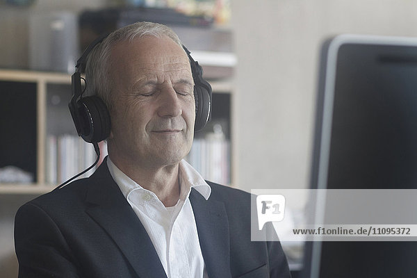 Älterer Geschäftsmann  der im Büro mit Kopfhörern Musik hört  Freiburg im Breisgau  Baden-Württemberg  Deutschland