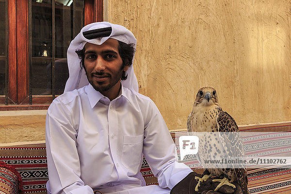 Sitzender Mann in traditioneller Kleidung entspannt sich mit seinem Falken auf dem Falken-Souq  Doha  Katar  Naher Osten