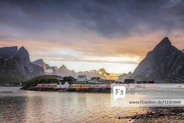 Sonnenuntergang über dem Fischerdorf  umrahmt von felsigen Gipfeln und dem Meer  Sakrisoya  Bezirk Nordland  Lofoten  Arktis  Nordnorwegen  Skandinavien Europa
