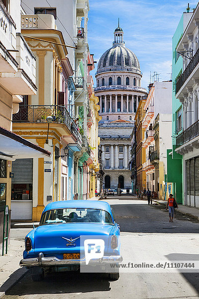 Ein Oldtimer geparkt auf der Straße neben kolonialen Gebäuden mit dem ehemaligen Parlamentsgebäude im Hintergrund  Havanna  Kuba  Westindien  Karibik  Mittelamerika