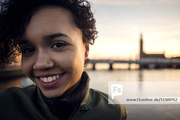 Porträt eines lächelnden Teenagermädchens mit lockigen  kurzen Haaren am Kanal in der Stadt.