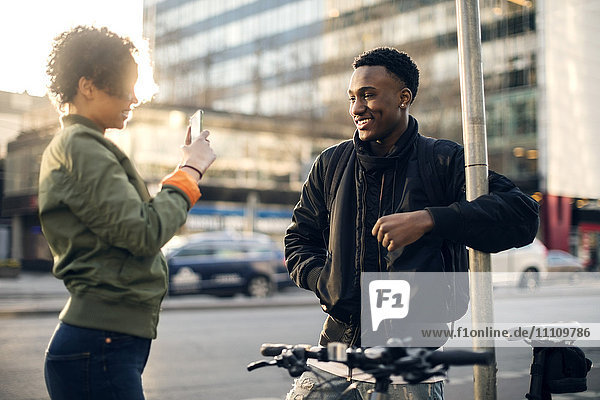 Seitenansicht eines Teenagers  der einen Freund über ein Smartphone fotografiert  während er an der Stadtstraße steht.