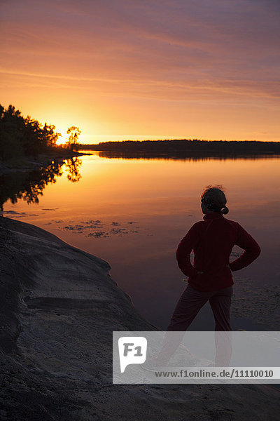 Rückansicht der Frau die bei Sonnenuntergang auf dem See gegen den Himmel steht.