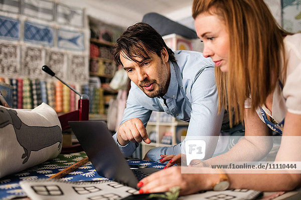 Male and female owners using laptop in fabric shop