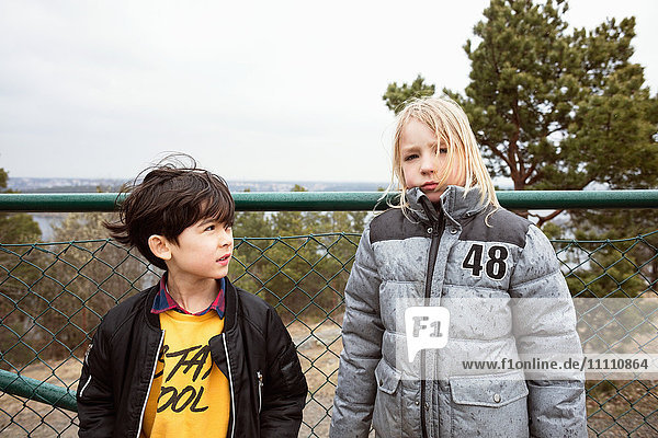Male and female students wearing warm clothing standing against fence