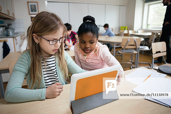 Serious students looking at digital tablet while sitting in classroom