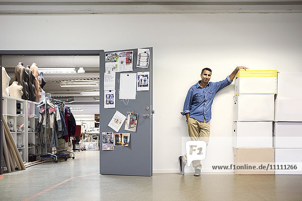 Full length of man standing by cardboard boxes at entrance of workshop