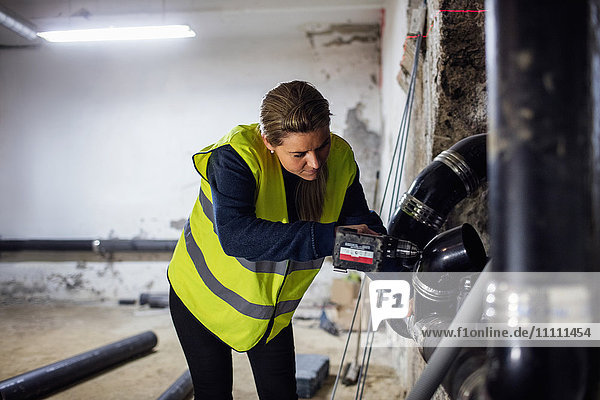 Concentrated female plumber sawing pipe at basement