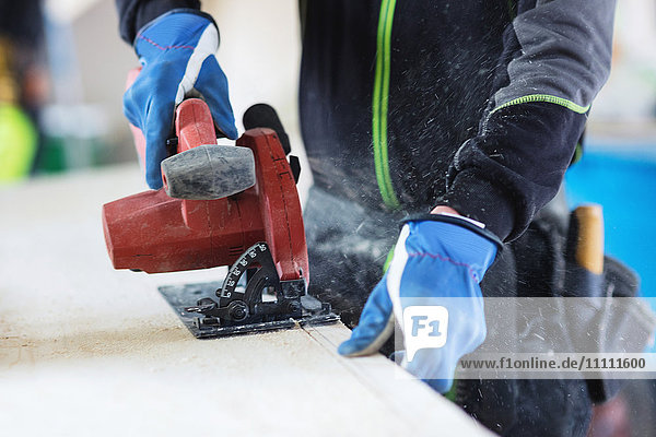 Midsection of manual worker using jigsaw on wooden planks at site
