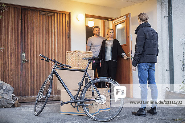 Man looking at parents while standing with cardboard boxes and bicycle at house entrance