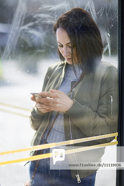 Frau an der Bushaltestelle mit Mobiltelefon