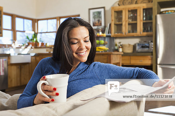 Hispanische Frau trinkt Kaffee und liest Zeitung