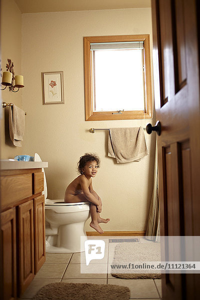 Nacktes gemischtrassiges Kleinkind auf der Toilette