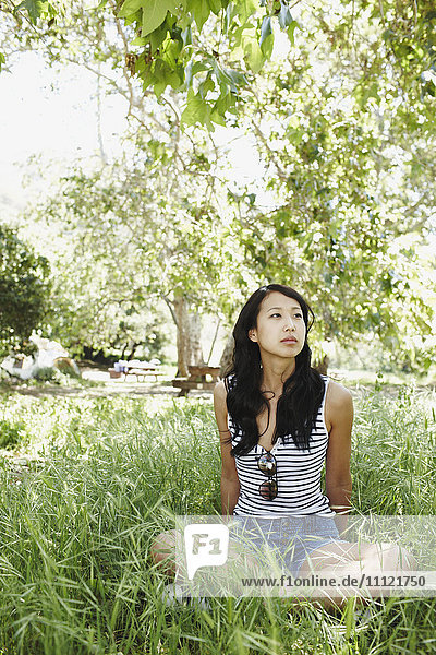 Asian woman sitting cross-legged in grass