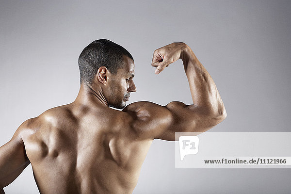 Bare chested mixed race man flexing biceps