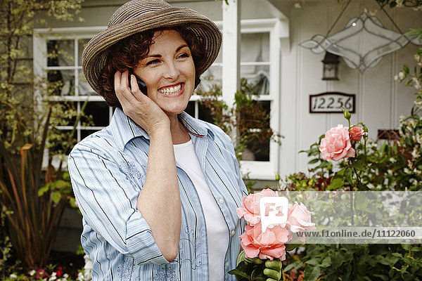Lächelnde Frau  die im Garten mit ihrem Handy telefoniert