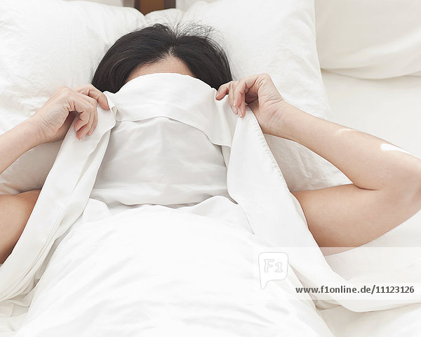 Hispanic woman in bed covering her face