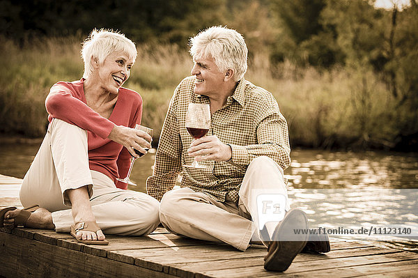 Older Caucasian couple having wine on wooden dock