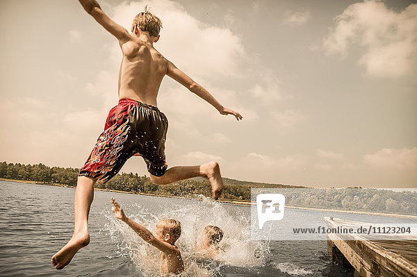 Caucasian boys jumping off wooden dock