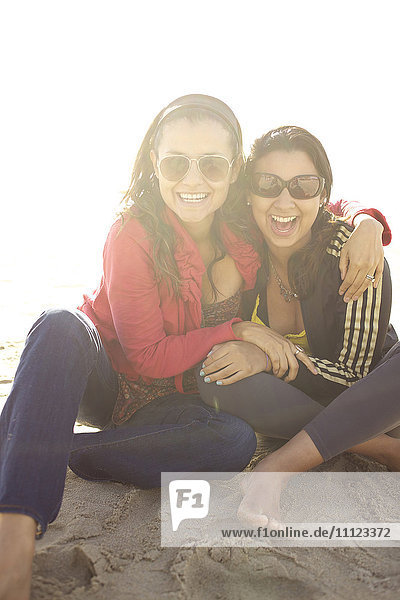 Smiling mixed race sisters sitting on beach