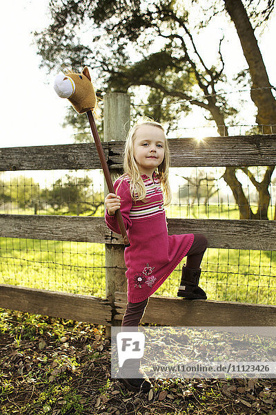 Caucasian girl holding stick horse near fence