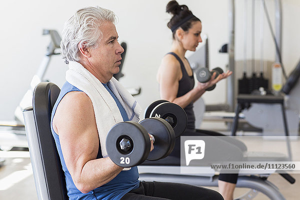 Older Hispanic man lifting weights in gym