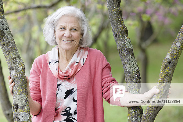 Lächelnde ältere kaukasische Frau,  die in der Nähe eines Baumes steht