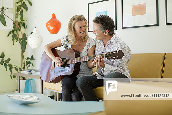 Mann bringt Frau im Wohnzimmer das Gitarrenspiel bei