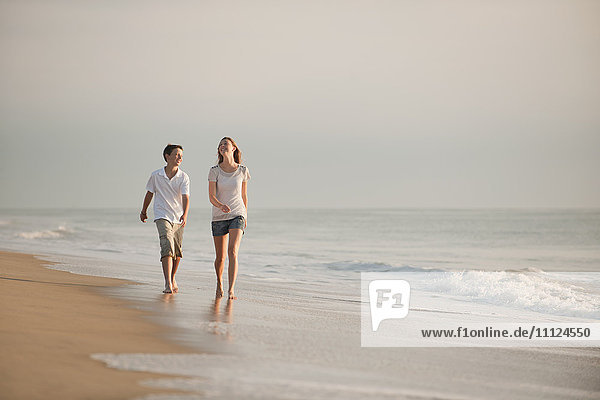 Kaukasischer Bruder und Schwester gehen am Strand spazieren