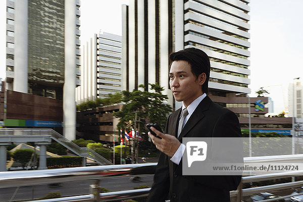 Asian businessman text messaging on cell phone outdoors