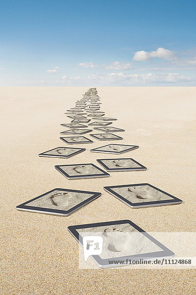Fußabdrücke auf Tablet-Computern im Sand