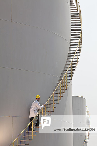Caucasian worker climbing staircase on storage tank