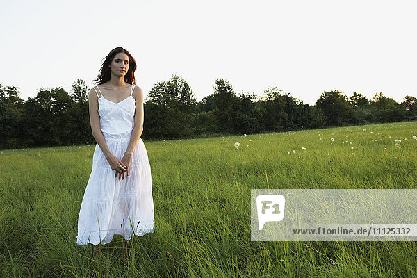 Woman standing in meadow with hands clasped