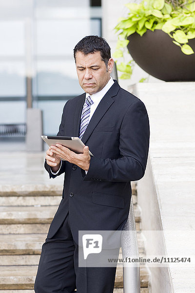 Hispanic businessman with tablet computer on city street
