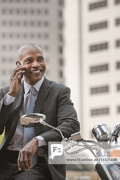 Black businessman sitting on scooter talking on cell phone