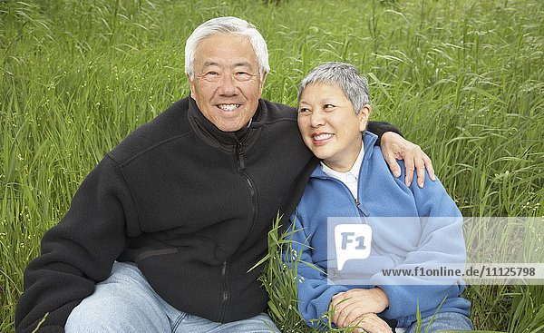 Älteres asiatisches Paar sitzt lächelnd im hohen Gras
