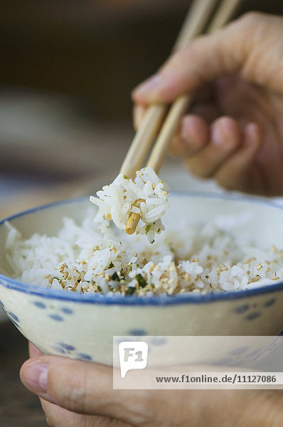 Person eating bowl of rice with chopsticks