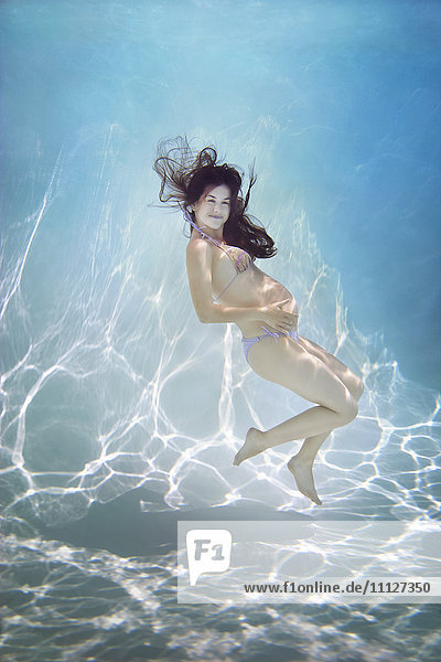 Schwangere kaukasische Frau schwimmt unter Wasser